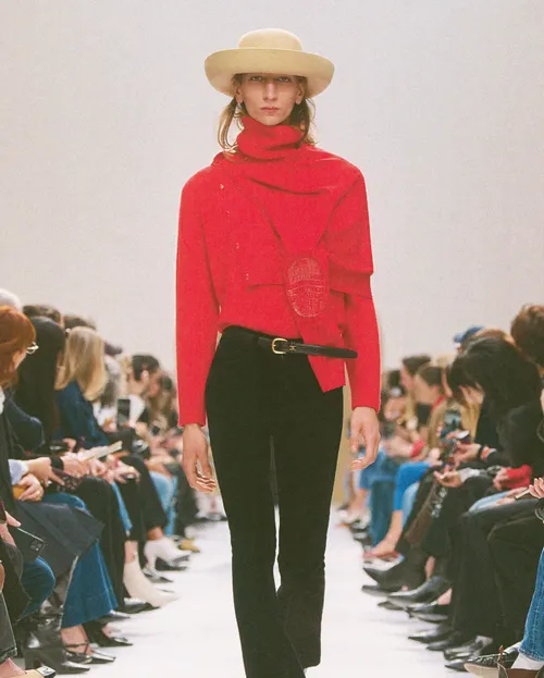 Celine FW2026 röd tröja med hög krage, svarta byxor och ljus hatt